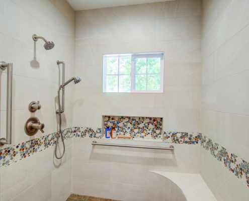 A roll-in shower features two shower heads, multiple hand railings, and a bench.